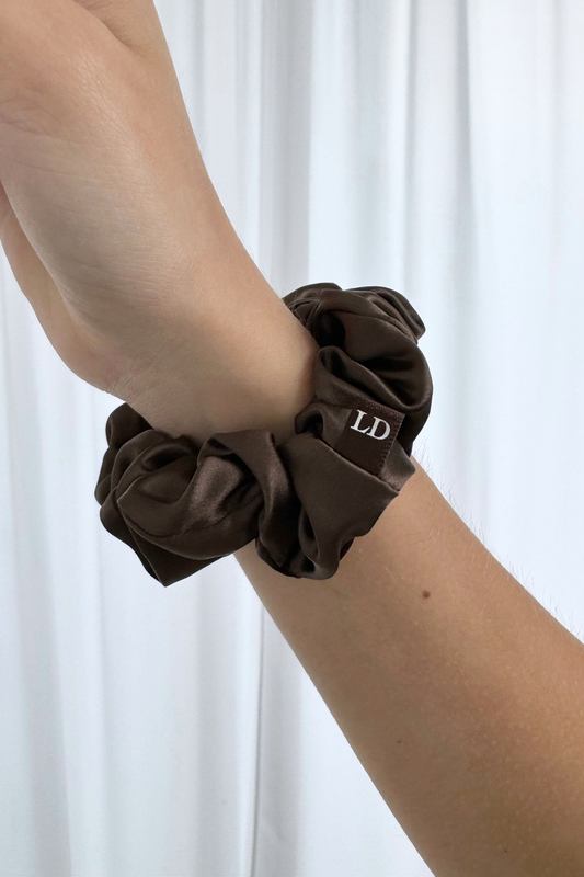 Brown silk scrunchie on a person's wrist with a white background
