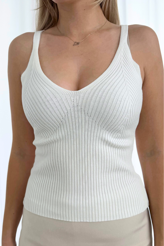 Woman wearing a white ribbed tank top against a plain background