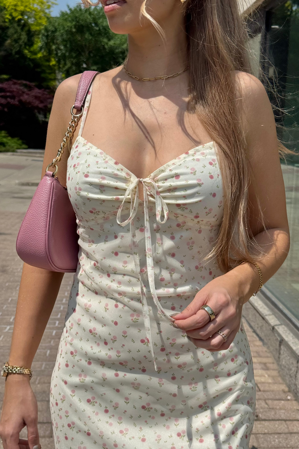 Woman wearing a floral yellow midi dress with a pink handbag outdoors