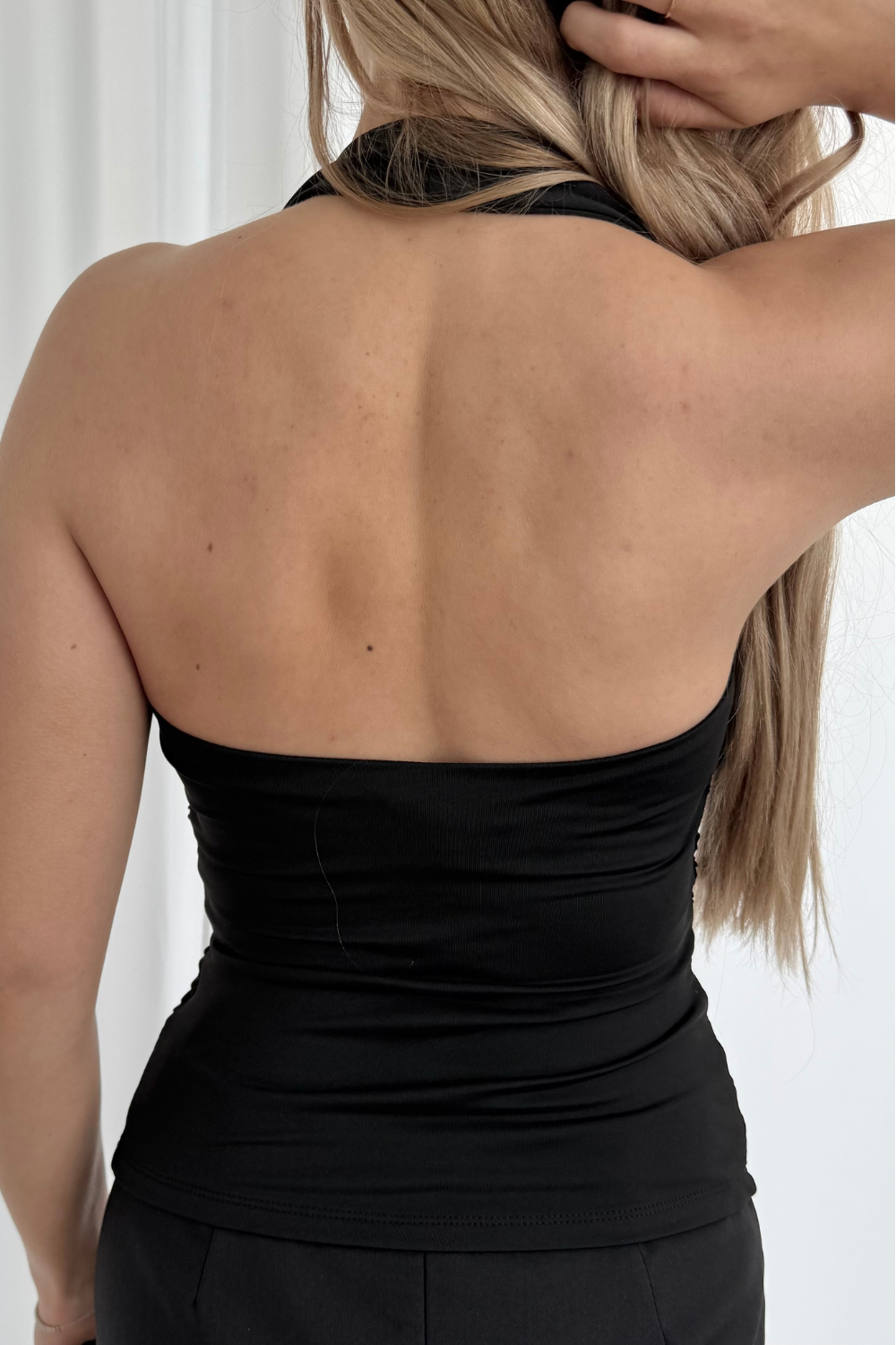 Person wearing a black halter top with a plain background