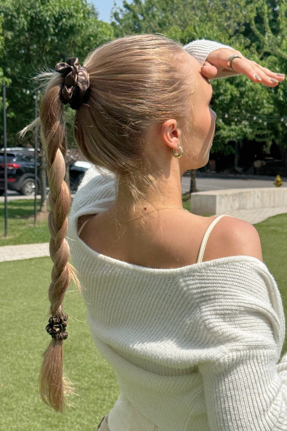 Woman with a braid and silk scrunchies wearing a white sweater outdoors on a sunny day