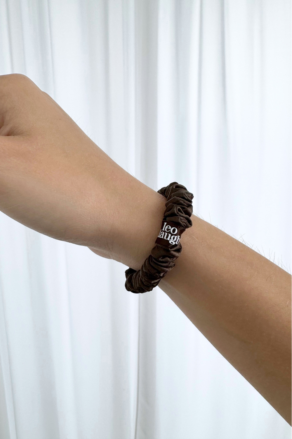 Brown silk scrunchie on a wrist with a white background